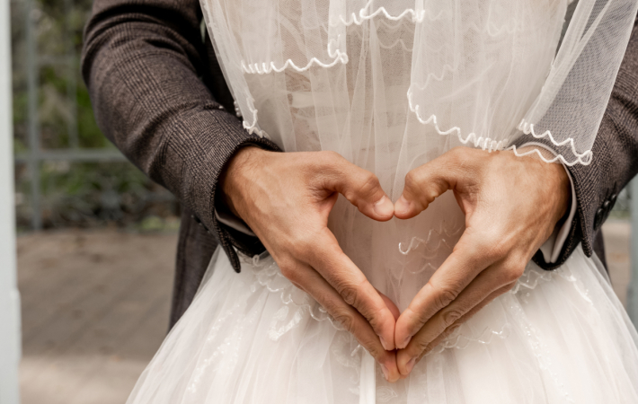 cropped view of man showing heart sign with hands while hugging bride, banner